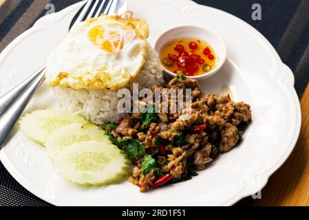 Classic Thai food spicy menu, Pad Kraprow or stir-fried minced pork with basils and chili, fried egg on white rice. Small bowl of fish sauce and chili Stock Photo