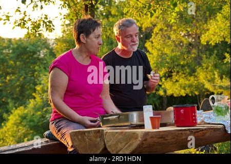 Senior couple sitting at the table in nature and eating Stock Photo