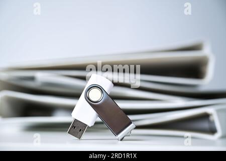 Usb flash drive stick in front of a heap of white file folders or ring binders, concept for space and paper saving digitalizing in office, archive, ad Stock Photo