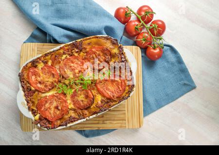 Lasagna, casserole with layered pasta, Bolognese beef sauce, vegetables and tomatoes, topped with melted cheese on a wooden kitchen board and a blue n Stock Photo