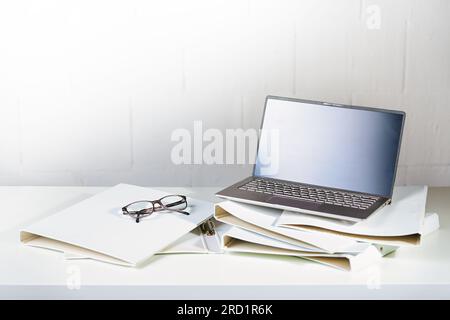 Laptop and glasses on several white ring binders on an office desk, administration and business work concept, copy space, selected focus, narrow depth Stock Photo