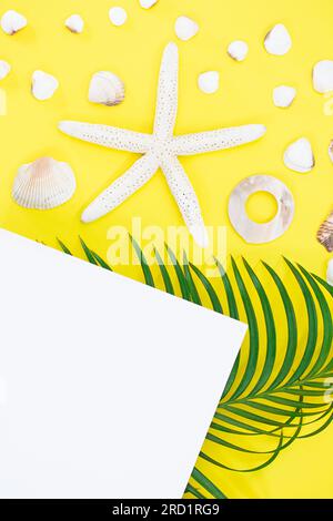 White starfish, shells with palm leaves and paper for text on side on yellow background. Flat lay. Travel, vacation, summer. Copy space Stock Photo