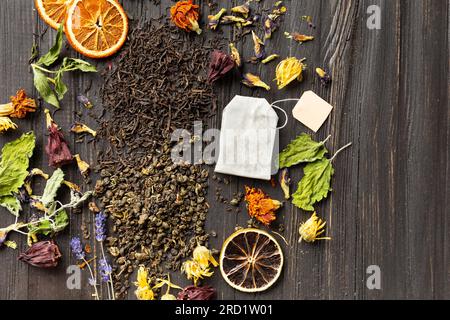 Composition of dry black and green tea, tea bag, dried citrus slices and dry hibiscus flowers on a dark wooden background top view. Stock Photo