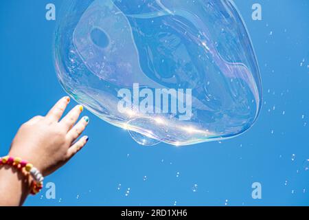 Hand of a child trying to catch some soap bubbles that rise to the sky Stock Photo