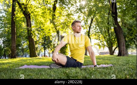 Man doing morning yoga at park outdoors in summer time. Guy stretching his back at nature in sunny day Stock Photo