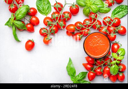 Freshly squeezed tomato juice in a glass and red cherry tomatoes on branches with green basil on gray table, food background, top view Stock Photo