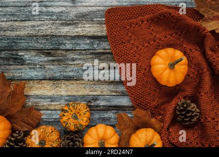 Warm and cosy handmade blanket with pumpkins, cones and autumn leaves on wooden background. Rustic fall flat lay composition with copy space. Stock Photo