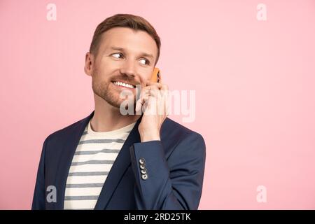 Happy guy in business jacket holding cellphone making call enjoy conversation isolated on pink blank Stock Photo
