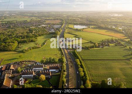 Aerial view of the A228 road cuttiing through fields in the Kent countryside with rows of Oast Houses in the bottom corner, in Kent, UK Stock Photo