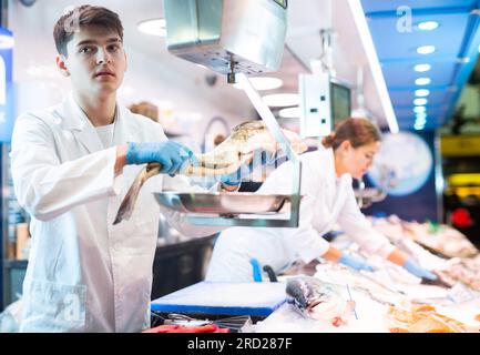 Skilful shop assistant weighing cod fish on scales in fish store Stock ...