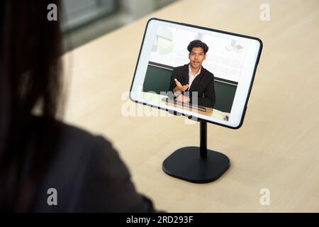 A focused woman is situated at a modern workspace, engrossed in tasks. Tablet computer is on the desk, it epitomizes a work from home setting. Stock Photo