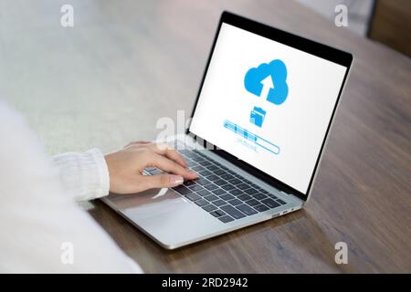 Woman uses her laptop showing a prominent cloud icon, a symbol for cloud computing services; represents adaptability to new-age tech solutions. Stock Photo