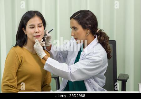 A professional healthcare provider is precisely performing a chin diagnosis procedure on a female patient in a sanitized, clinical environment. They a Stock Photo