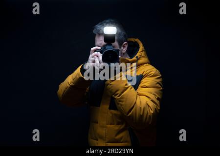 Photographer in a yellow coat taking a photo with flash with a black background Stock Photo