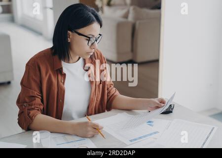 Serious business lady is examining documents. Young caucasian woman working remote from home. Manager or entrepreneur doing paperwork. Concept of inte Stock Photo