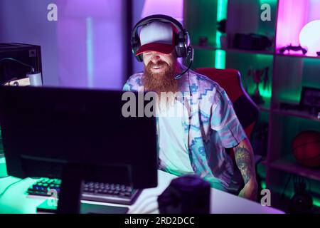 Young redhead man streamer playing video game using computer at gaming room Stock Photo