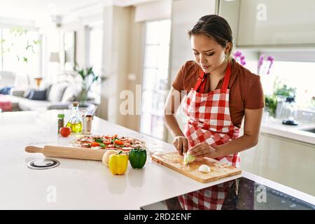 Young beautiful hispanic woman cutting onion crying at the kitchen Stock Photo