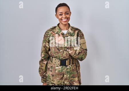 Beautiful african american woman wearing camouflage army uniform cheerful with a smile on face pointing with hand and finger up to the side with happy Stock Photo
