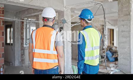 Two men builders standing together backwards at construction site Stock Photo