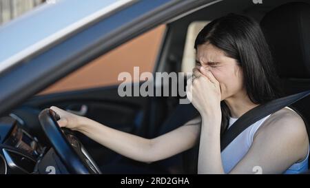 Young beautiful hispanic woman tired sitting on car yawning at street Stock Photo