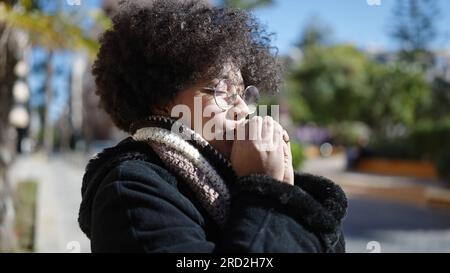 Young african american woman wearing scarf for cold weather rubbing hands together at park Stock Photo