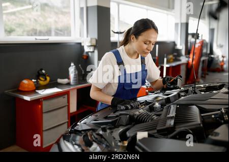 Young female tradesperson mechanic working on car engine in auto repair garage Stock Photo