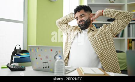 Young hispanic man student using laptop stretching back at library university Stock Photo