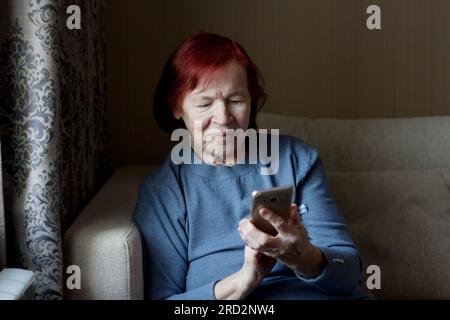 hands of an senior woman holding an old smartphone in her hands. Closeup, elderly man uses smartphone, touches screen of mobile phone with his finger. Stock Photo