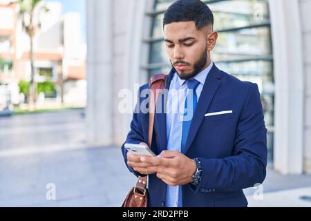 Young latin man business worker using smartphone with serious expression at street Stock Photo