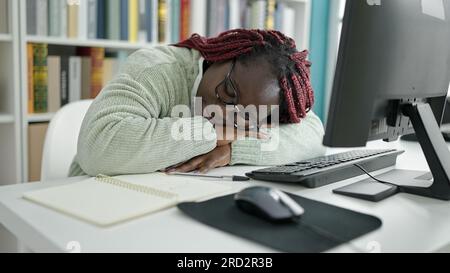 African woman with braided hair student sleeping by computer at university library Stock Photo