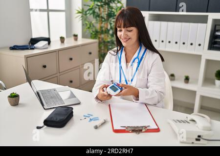 Young beautiful hispanic woman doctor smiling confident measuring glucose at clinic Stock Photo