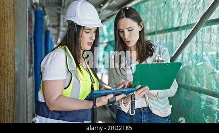 Two women architect and worker using touchpad and clipboard working at street Stock Photo