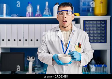 Young arab man working at scientist laboratory afraid and shocked with surprise and amazed expression, fear and excited face. Stock Photo