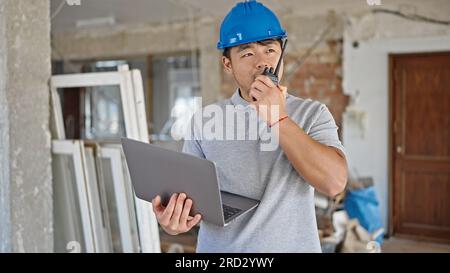 architect using laptop speaking on walkie talkie at construction site Stock Photo