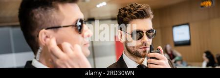 bodyguard service, private security, handsome man in sunglasses and formal wear communicating with his working partner by walkie talkie, hotel securit Stock Photo