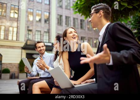 Group of employees, colleagues sitting on bench outside office, working, talking, discussing projects. Teamwork Stock Photo