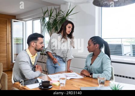 Young designer giving some new ideas about project to his partners in conference room. Businesspeople discussing over new business project in office. Stock Photo