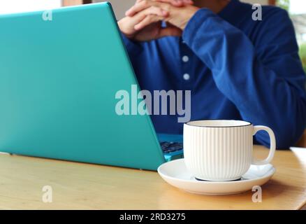 Closeup of a cup of coffee with a man working on laptop in the backdrop Stock Photo