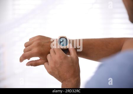 Man setting smart home control system via smartwatch against light background, closeup. App interface with icons on display Stock Photo