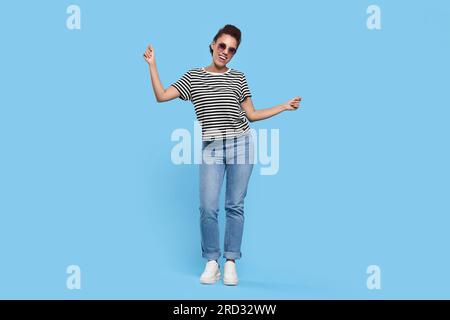 Happy young woman in stylish sunglasses dancing on light blue background Stock Photo