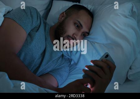 Young man using smartphone in bed at night. Internet addiction Stock Photo
