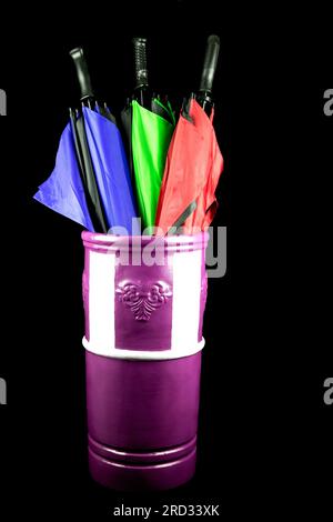 Coloured umbrellas in a painted earthenware umbrella stand isolated on a black background Stock Photo