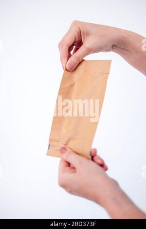 Close-up of women hands with a neat manicure opening a paper bag. A cosmetologist in a gray uniform tears open a bag of cosmetic tools. Doctor opens a Stock Photo