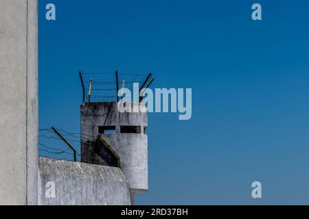 Old prison watchtower topped with barbed wire fencing Stock Photo