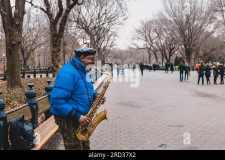 Busker playing saxophone while other passersby pass around him, Central Park, New York Stock Photo
