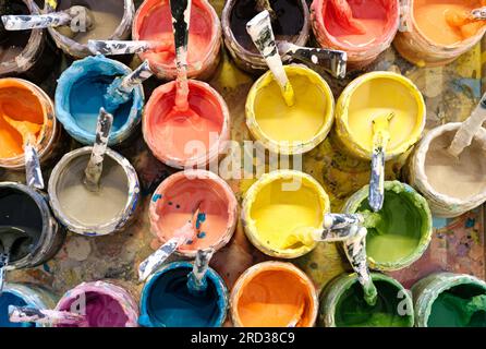 Large group of open old dirty cans of multi-colored paints, view from above, horizontal crop, abstract artistic background Stock Photo