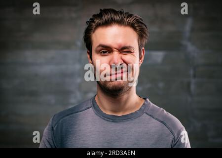 Young handsome man blinking portrait on gray wall background Stock Photo