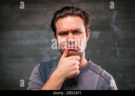 Young pensive man portrait on gray wall background Stock Photo