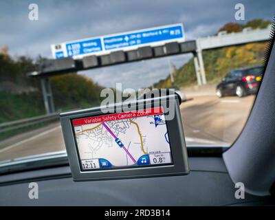 Satellite Navigation SAT NAV GPS screen in-car windscreen mounted, on M25 Orbital motorway with red 'Variable Safety Camera Zone' alert speed warning displayed Surrey UK Stock Photo