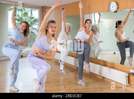 Group of excited young adult women in activewear performing dynamic movements during exercising together in fitness studio Stock Photo
